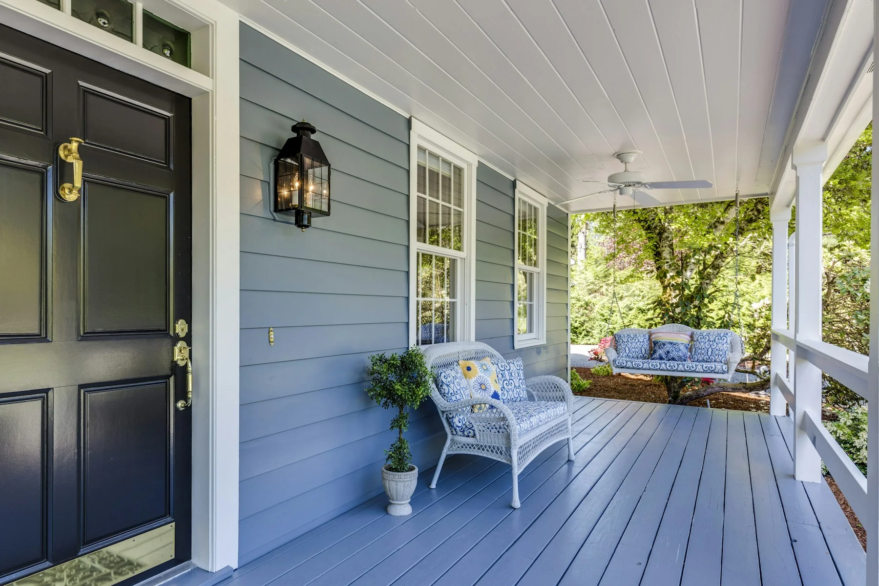 A black front door opening onto a blue covered porch with white wicker seating