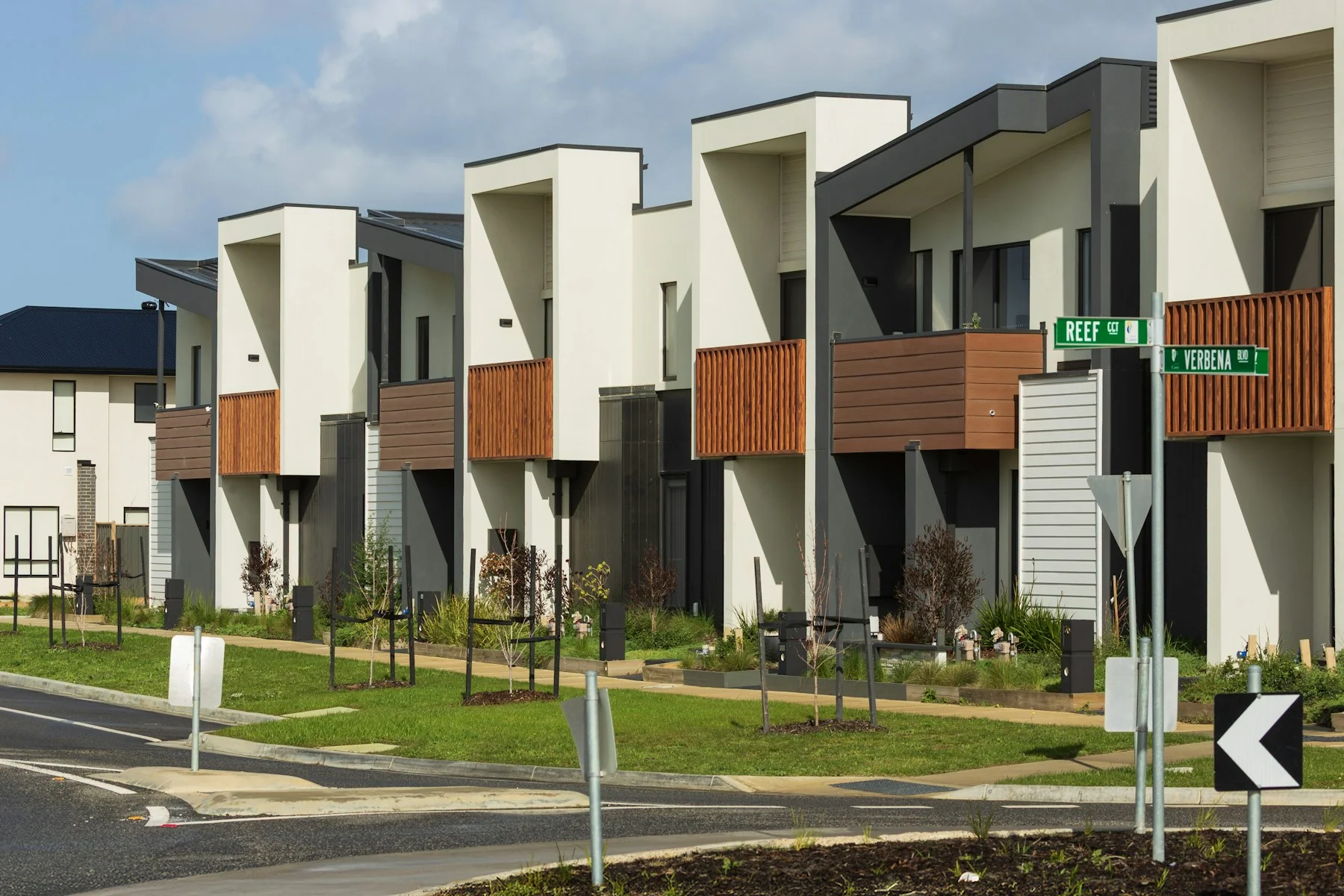 A row of modern townhouses with wooden balconies and landscaped front gardens