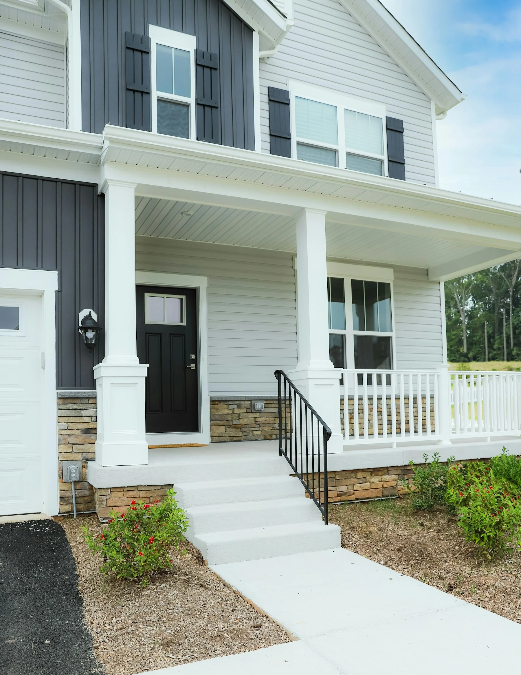 A white house with dark shutters, a black front door and a landscaped front porch