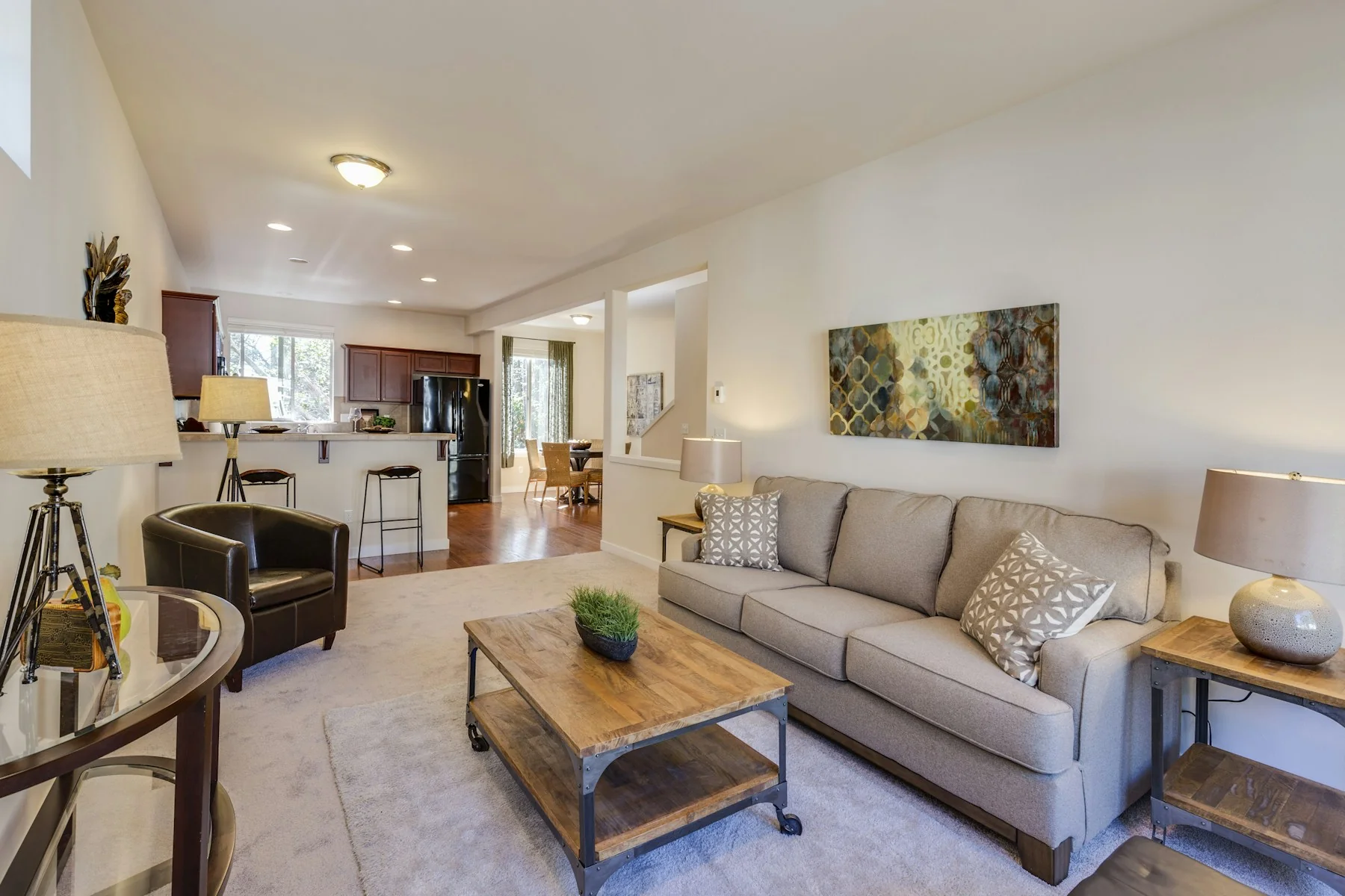 A staged living room with a neutral sofa, wooden coffee table and an open kitchen