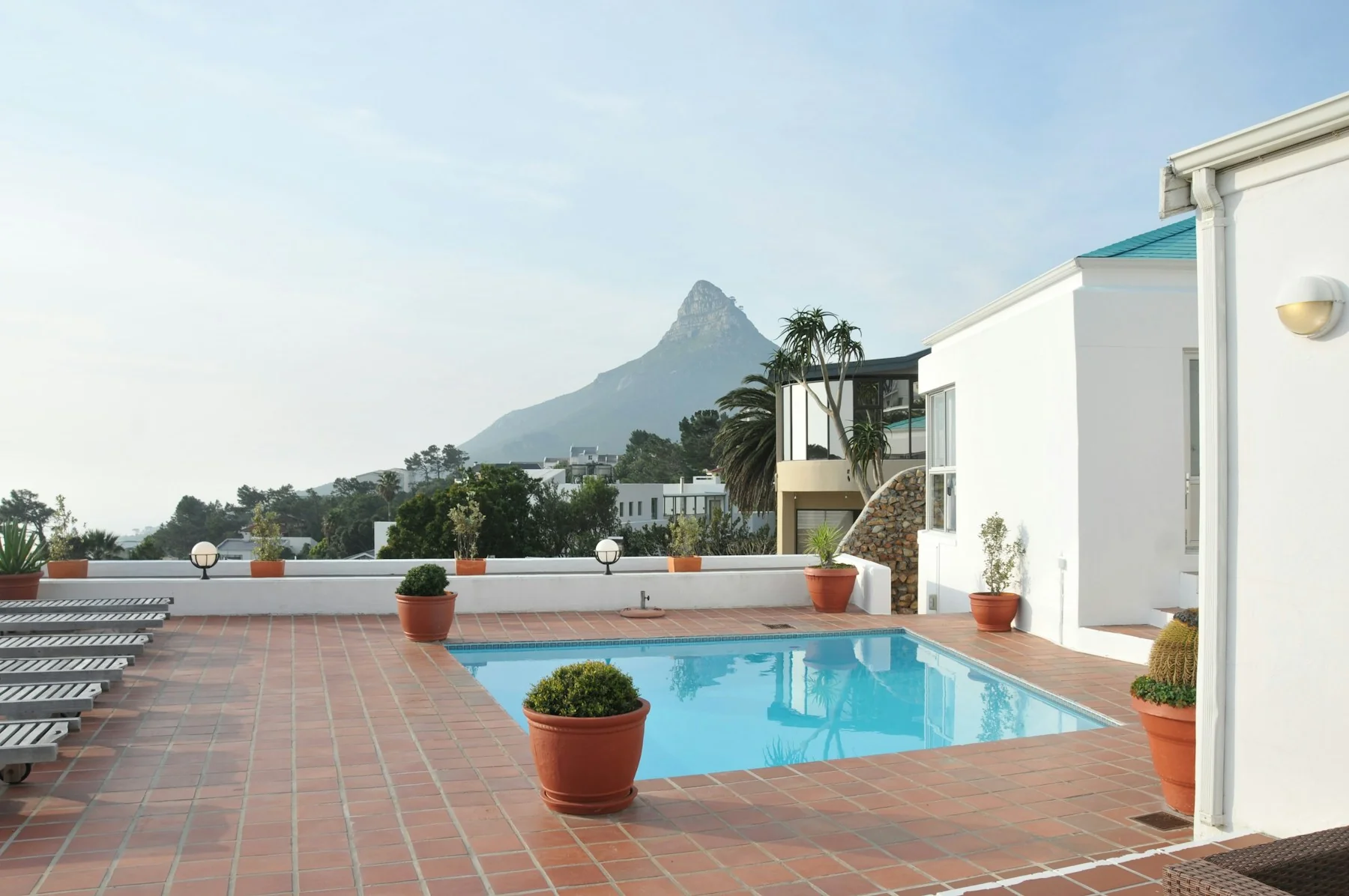 A sunlit swimming pool on a terracotta terrace beside a white building